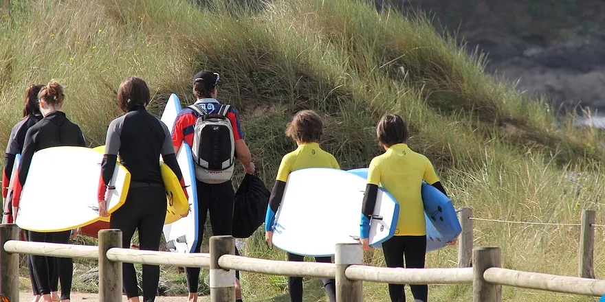 Des élèves descendent vers la plage, planches sous le bras
